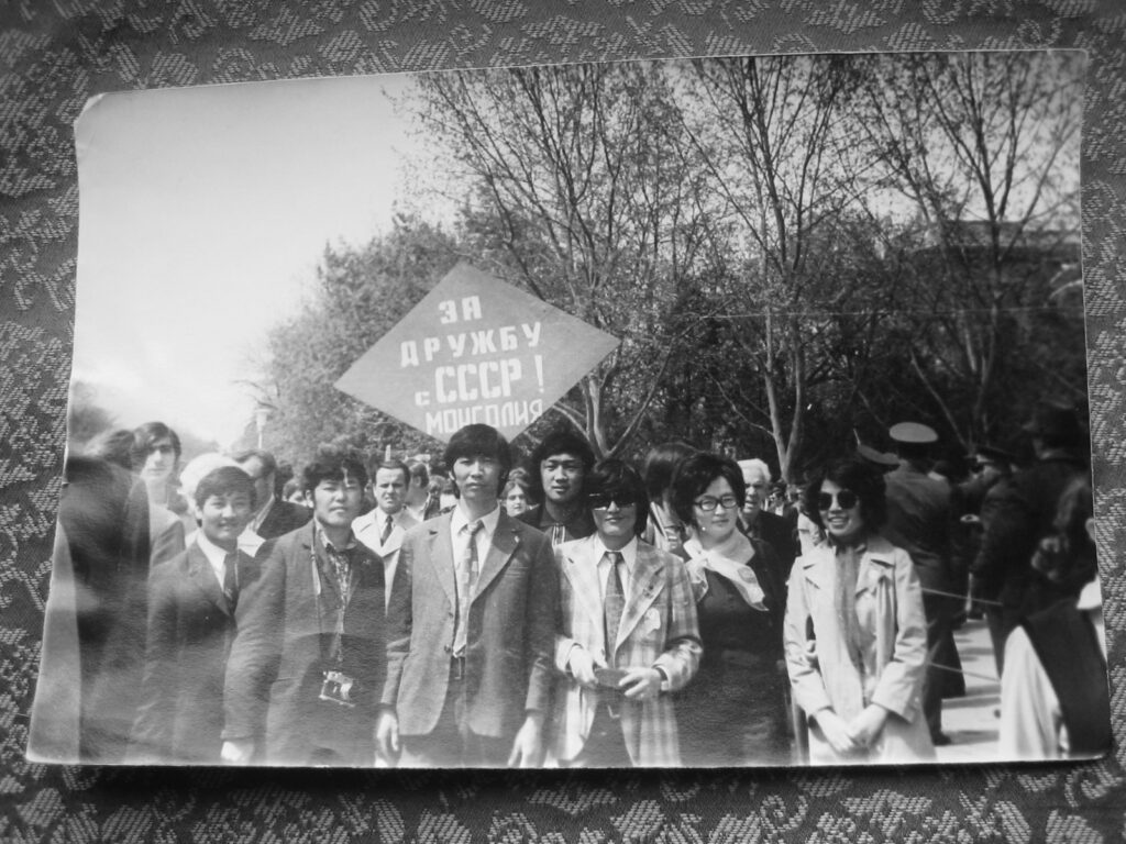 Handmaa (on the right) and her husband (third from right, front row) with other Mongolian “youth” whilst attending university in the City of Petigorsk. The sign written in Russian Cyrillic, not Mongolian Cyrillic reads, “in friendship with the USSR. Mongolia”. Photograph courtesy of J.Avrazed. Reprinted on CPinMongolia.com with permission.